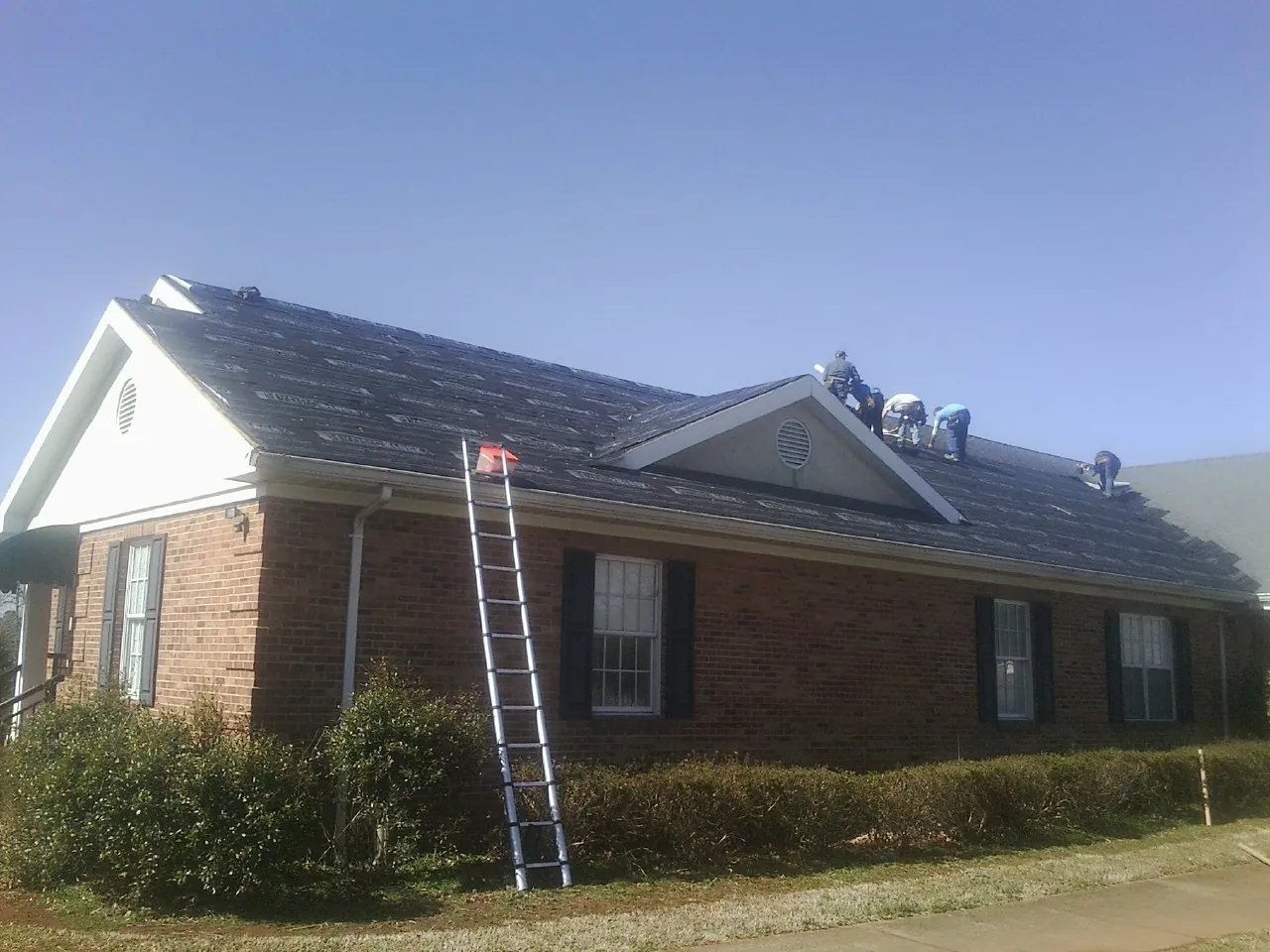 Crew tearing shingles off a brick ranch roof with a ladder set — Emergency Roof Repair work by our crew in Hampton Falls