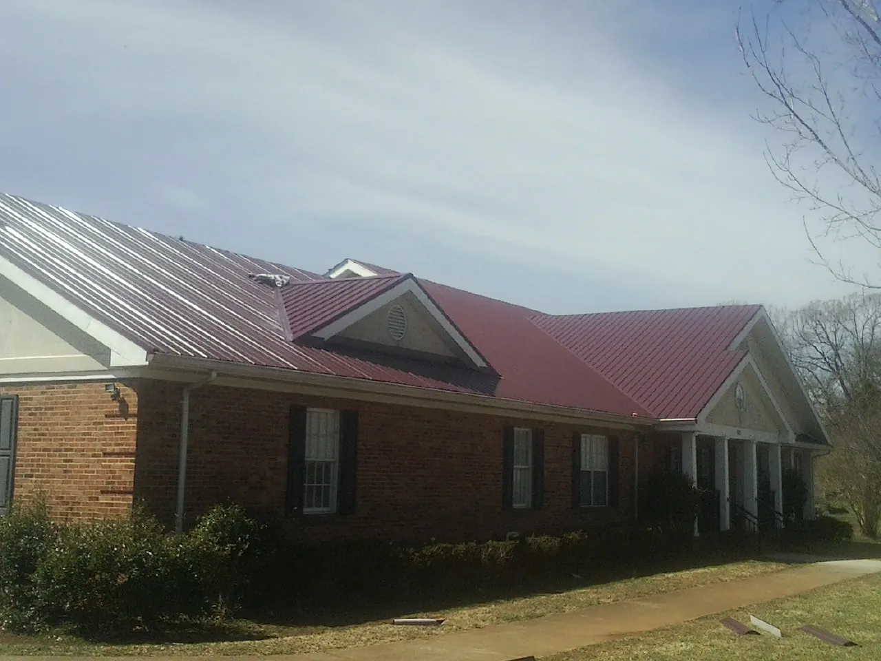 Red metal roof with gabled entries on a long brick building, from a Hail Damage Roof Repair job in Hampton Falls