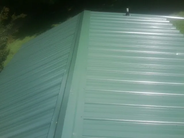 New green metal panels meeting at the ridge of a roof — Flat Roof Repair work by our crew in Hampton Falls