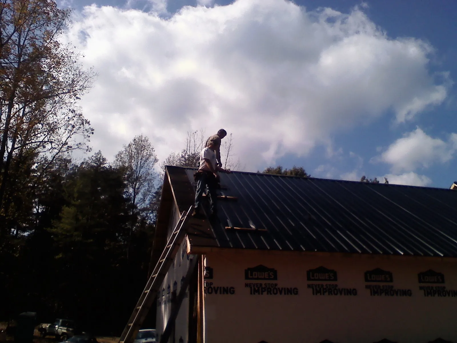 Roofer fastening dark metal panels high against a cloudy sky, from a Roof Inspection job in Hampton Falls