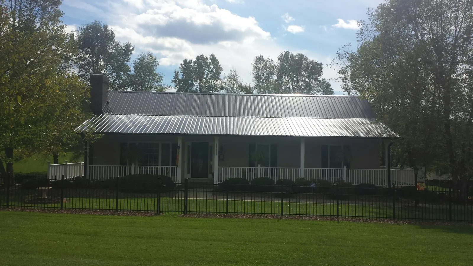 Gray metal roof on a brick ranch with a full width front porch — Gutter Guard Installation work by our crew in Hampton Falls